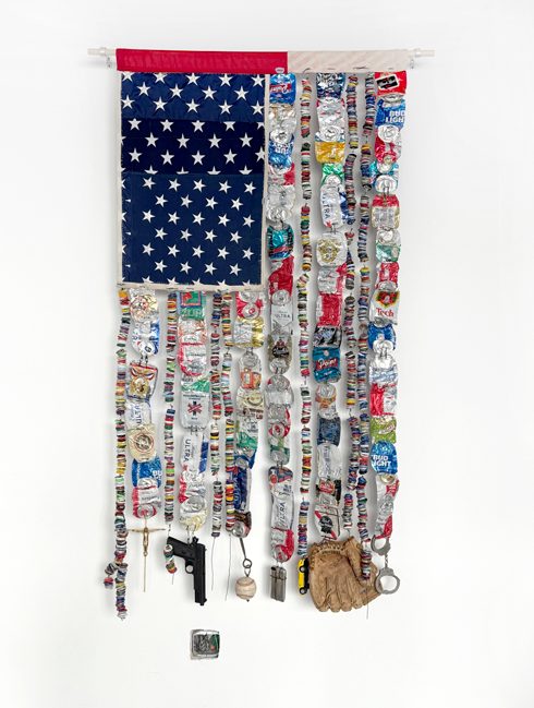 An assemblage work combining an American flag with dense strips of found objects and printed material.