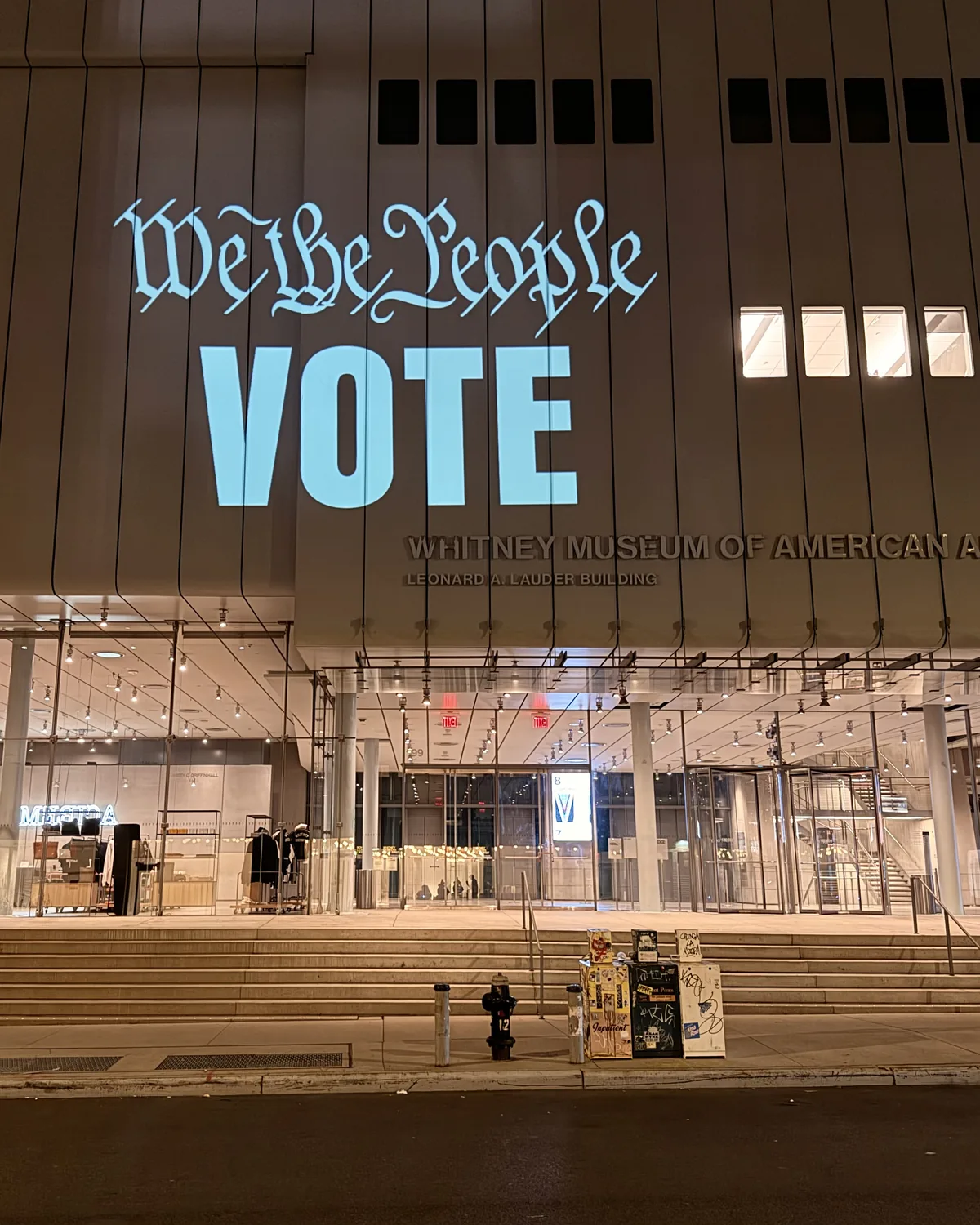 We the People VOTE in pale blue letters projected across the Whitney Museum&rsquo;s facade at night.